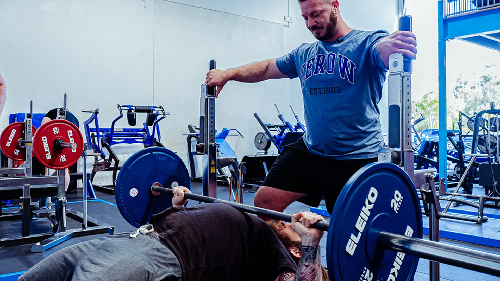 ZeroW powerlifting coach spotting an athlete's bench press in the gym